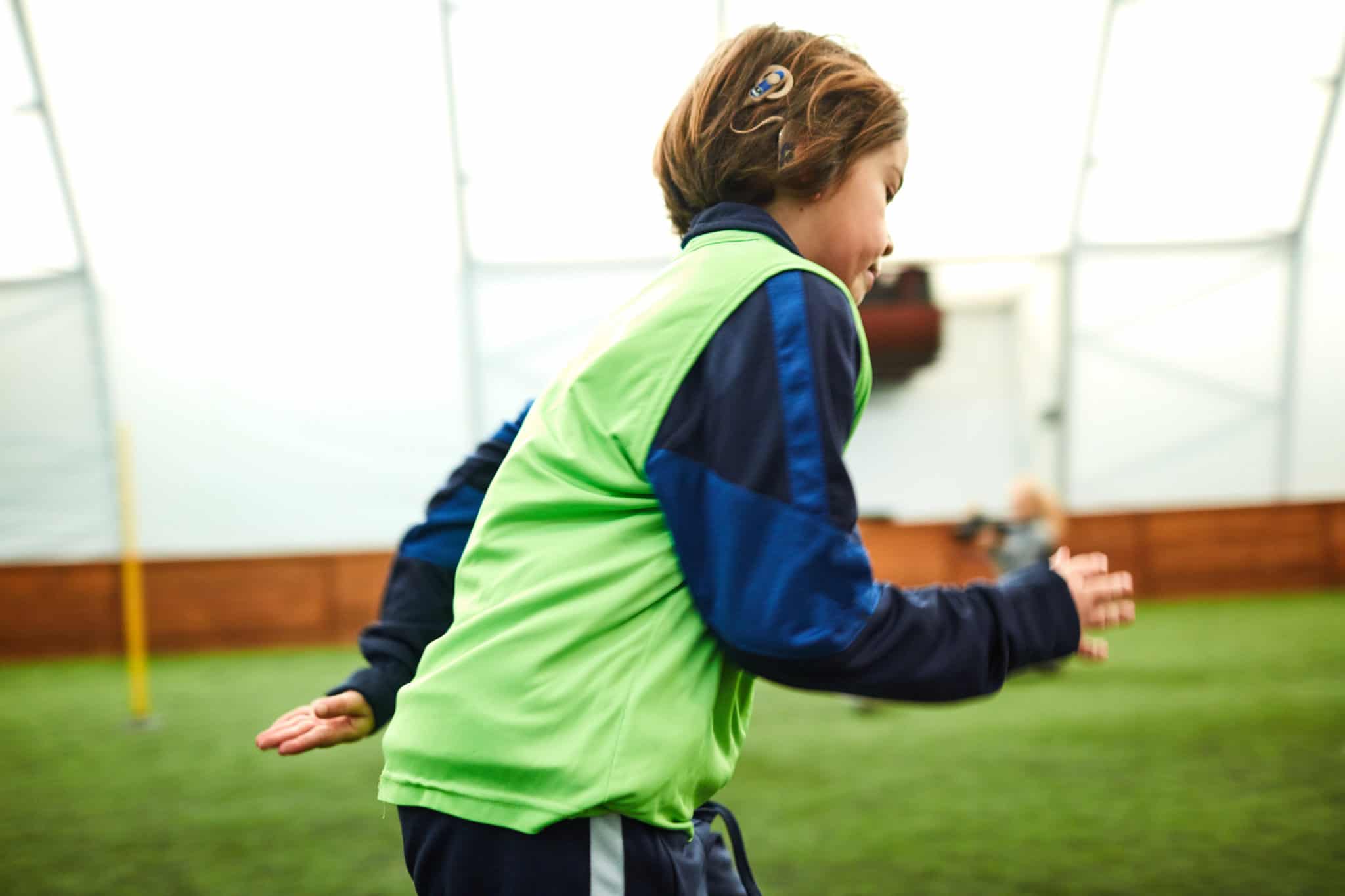 Boy with cochlear implant running on soccer field