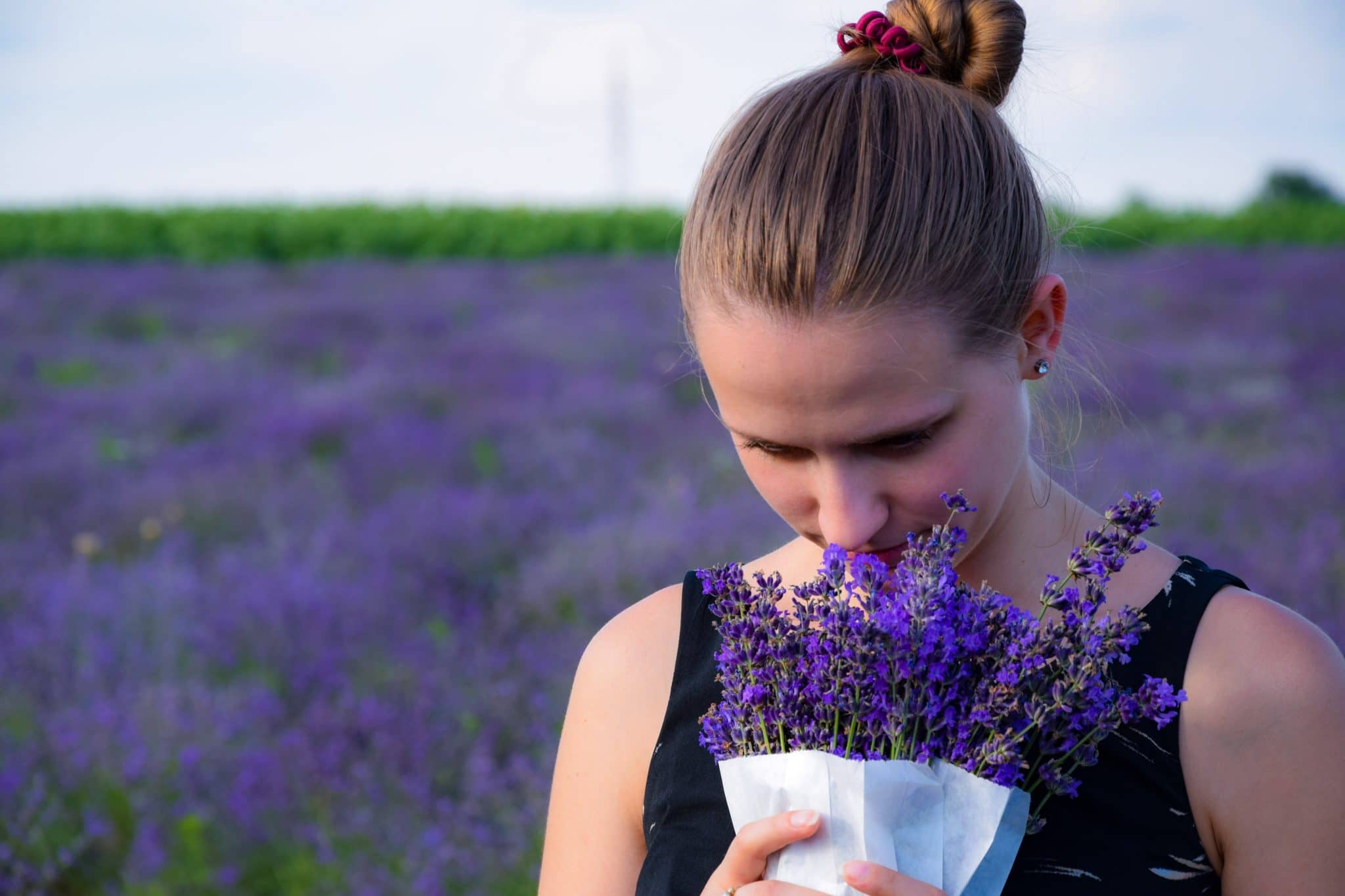 a woman smelling a bunch of lavender next to a field of lavender