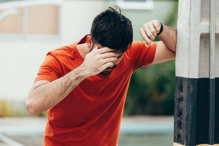 Man puts his hand on his face and leans on a pole in a reaction to dizziness 