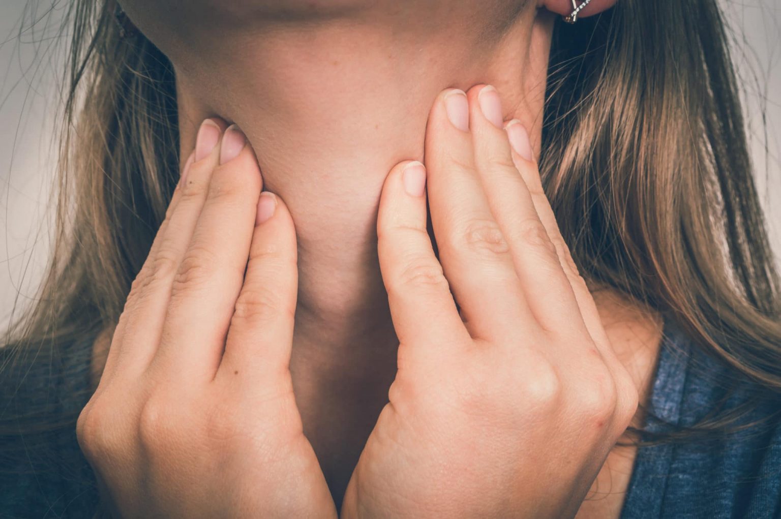 Close up of a woman with her finger tips on her neck checking her sore throat.