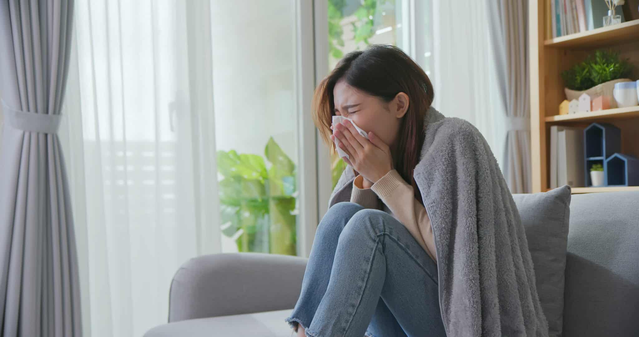 Woman sneezing while sitting on couch in pain.