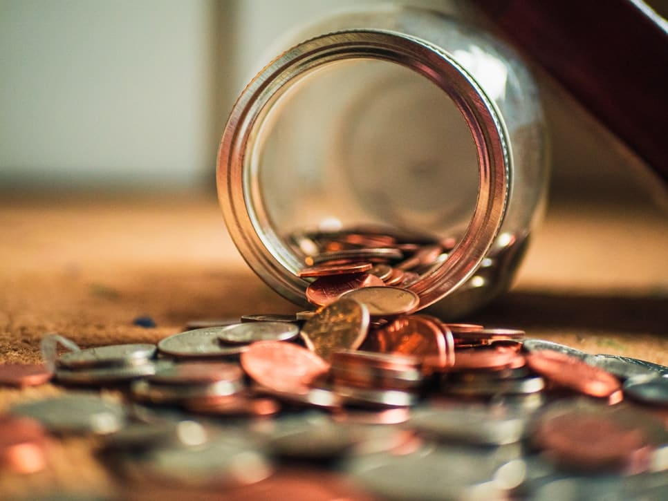 A pile of coins spilling out of a glass jar.