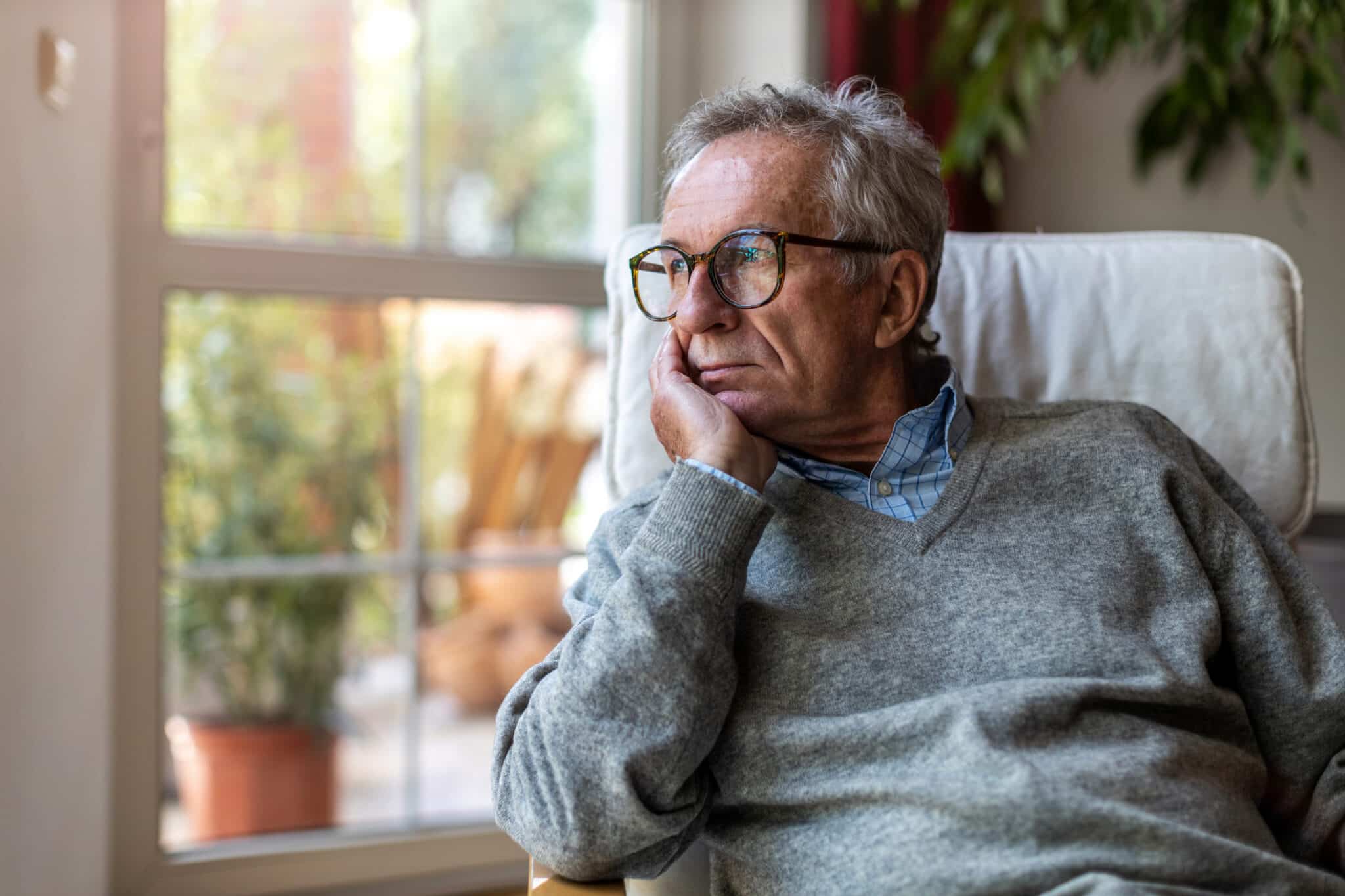 Senior man looking out of window at home.