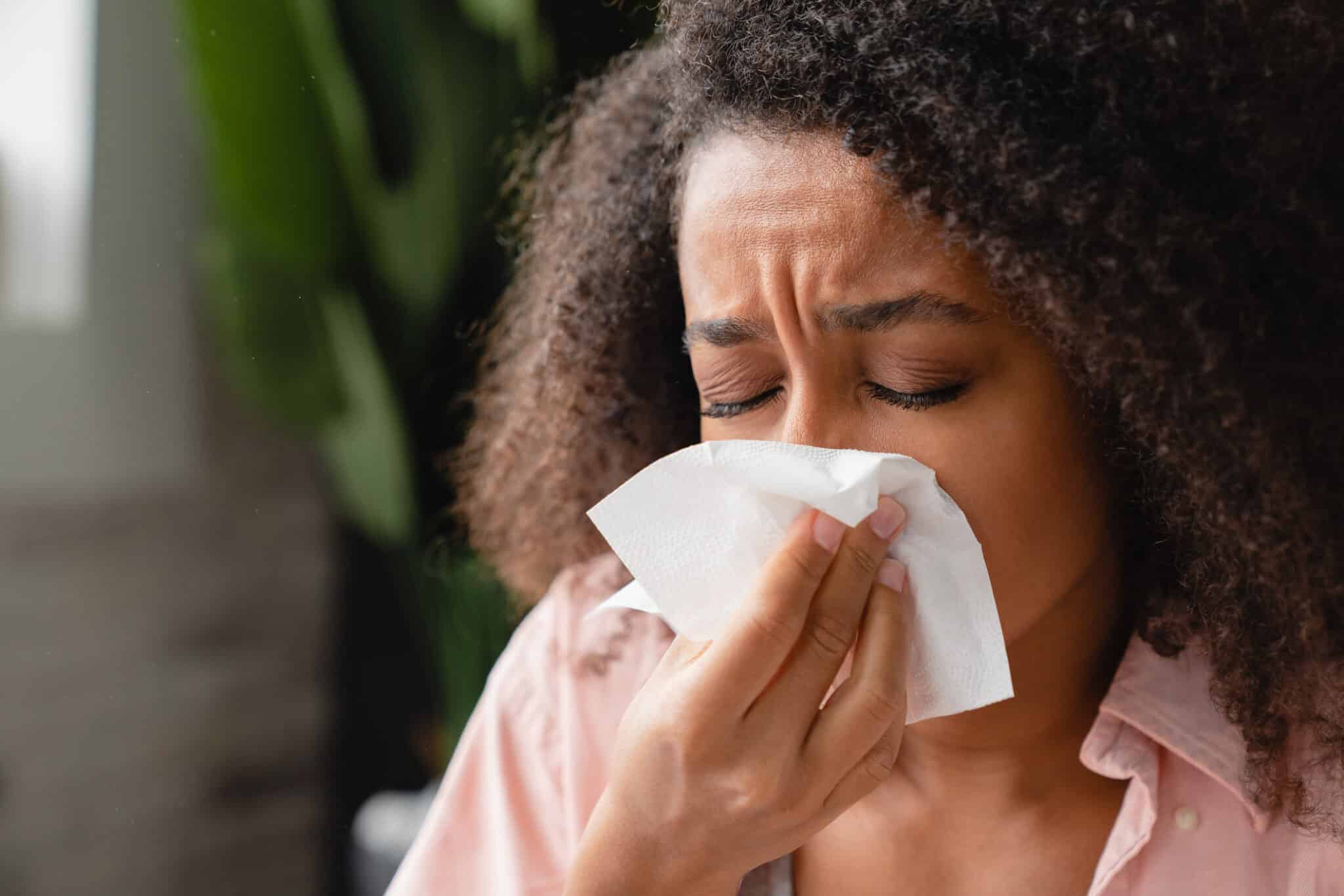 Woman with allergies sneezing into a tissue.