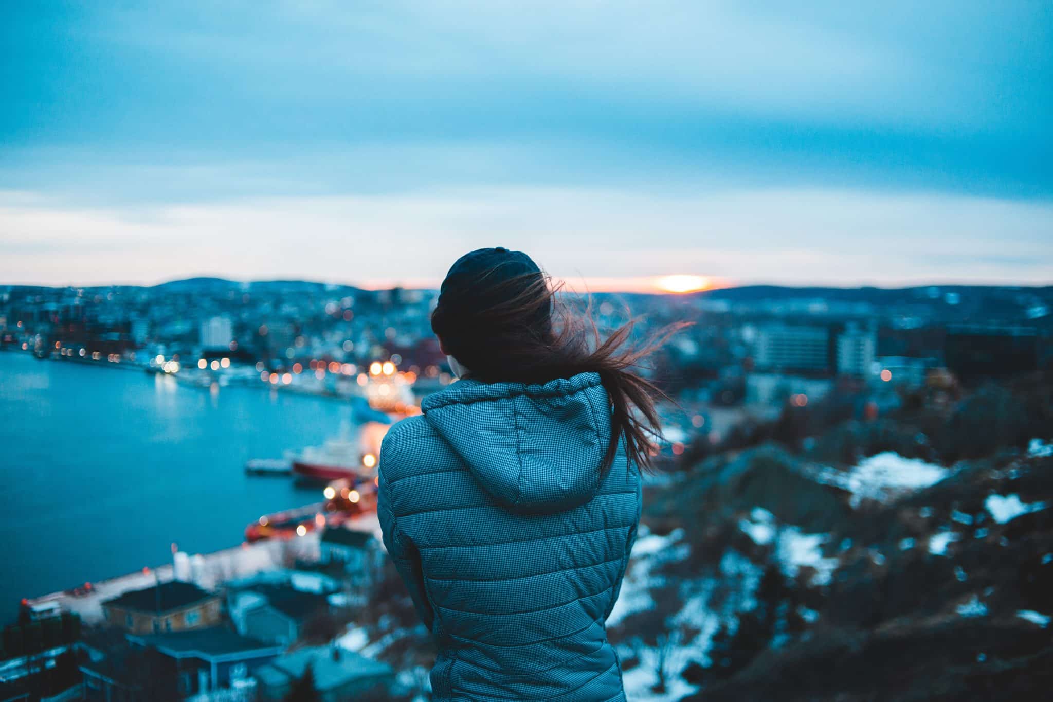 Woman standing on the top of a building looking out at the city on a windy day.