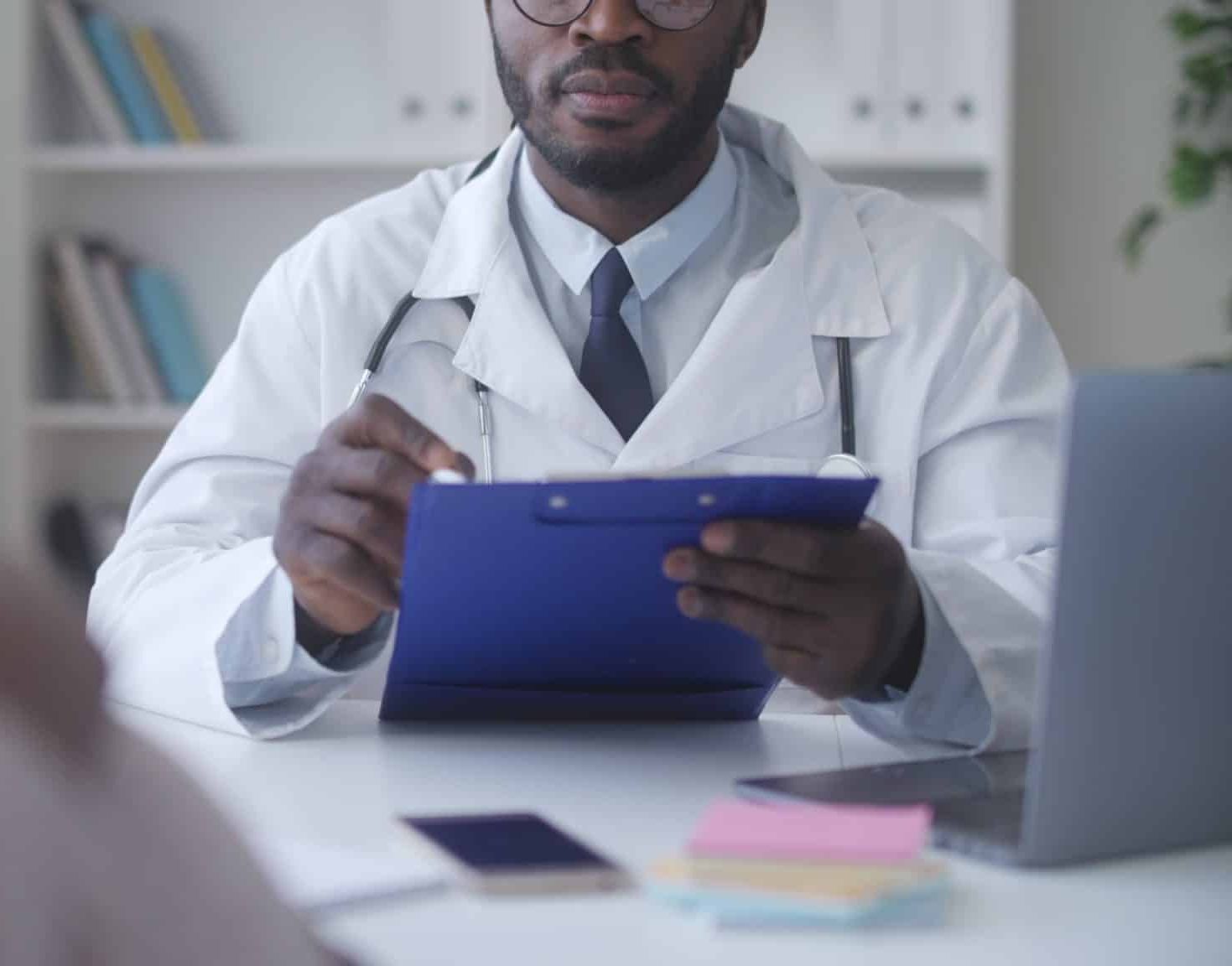 Doctor writing down notes while taking to patient.