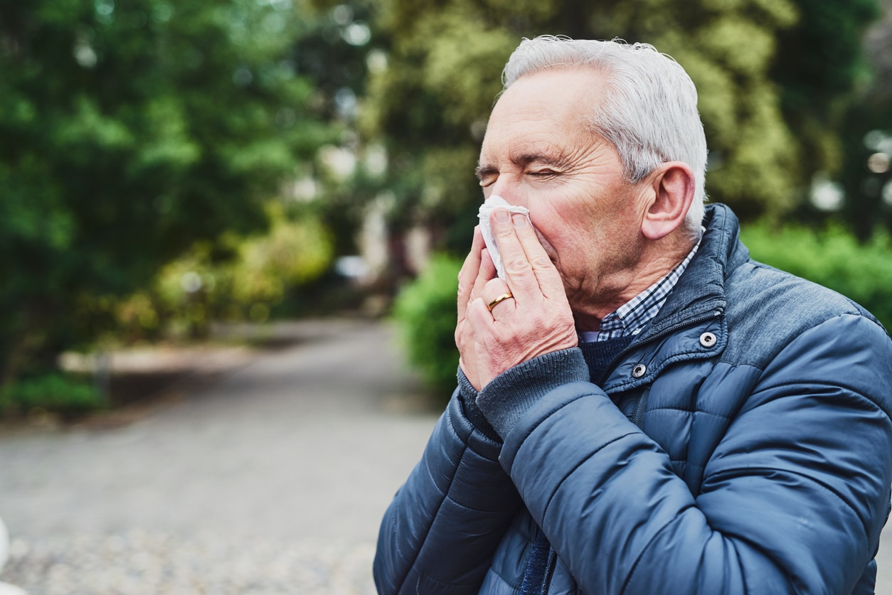 Senior man in the park blowing his nose into a tissue. 