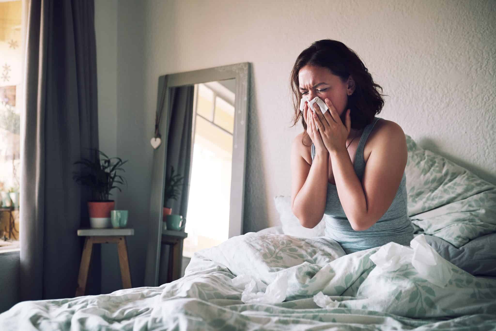 Woman with allergies blowing her nose in bed.