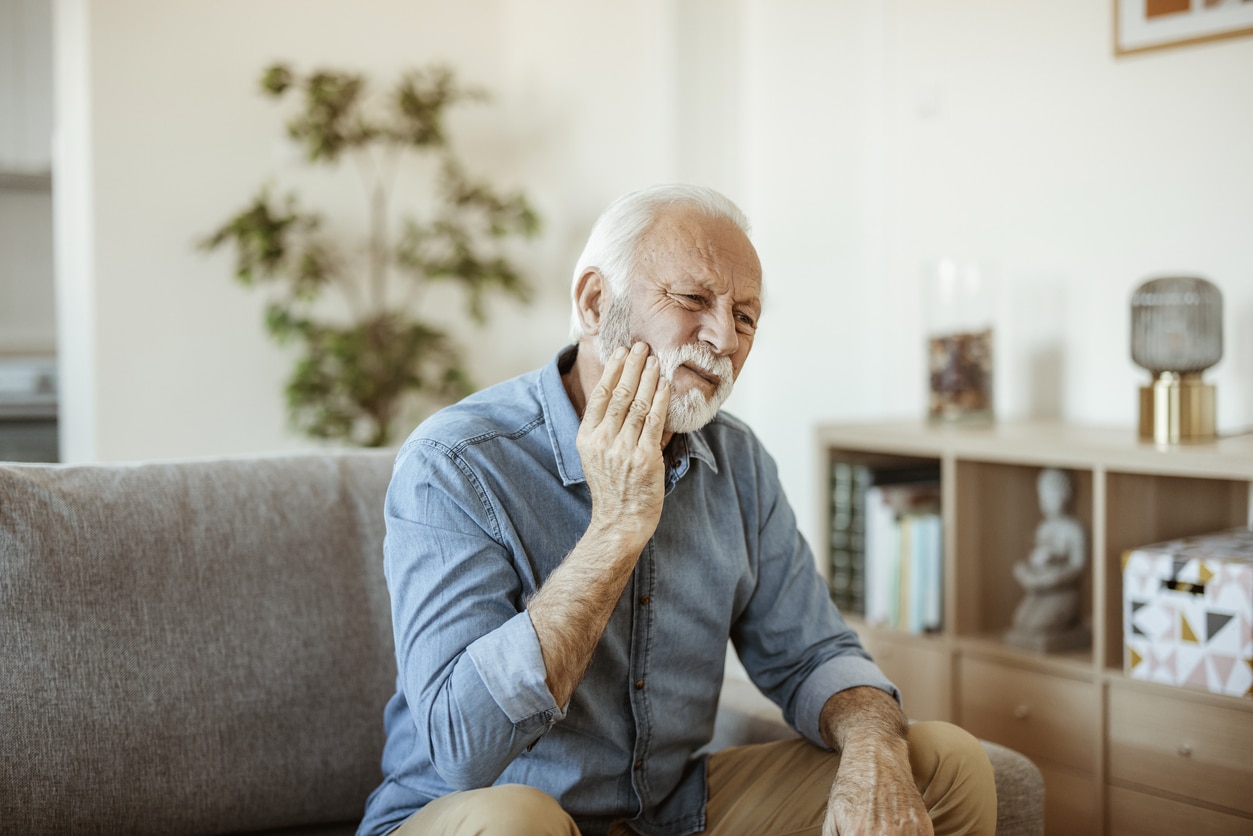 Senior man with toothache sitting on the couch holding his jaw