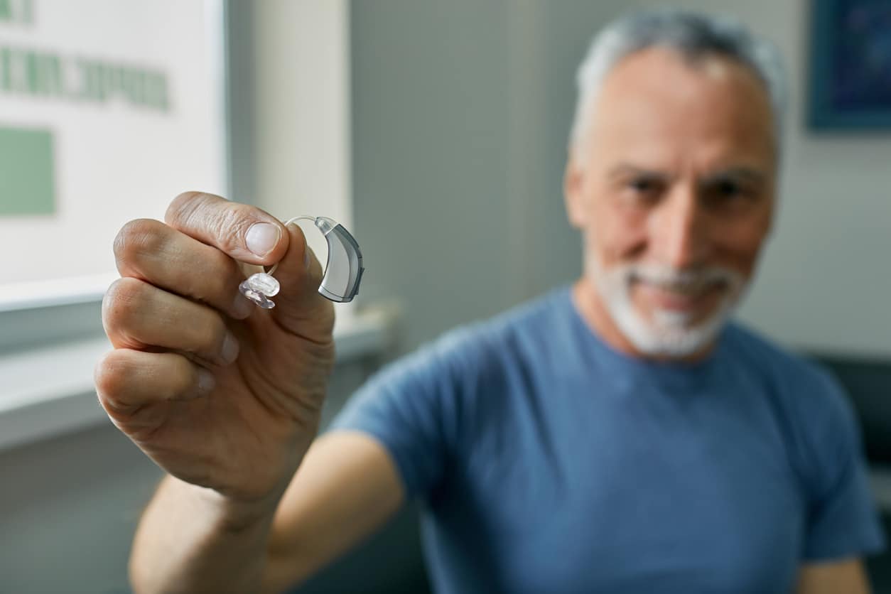 Senior man holding up a behind-the-ear hearing aid.