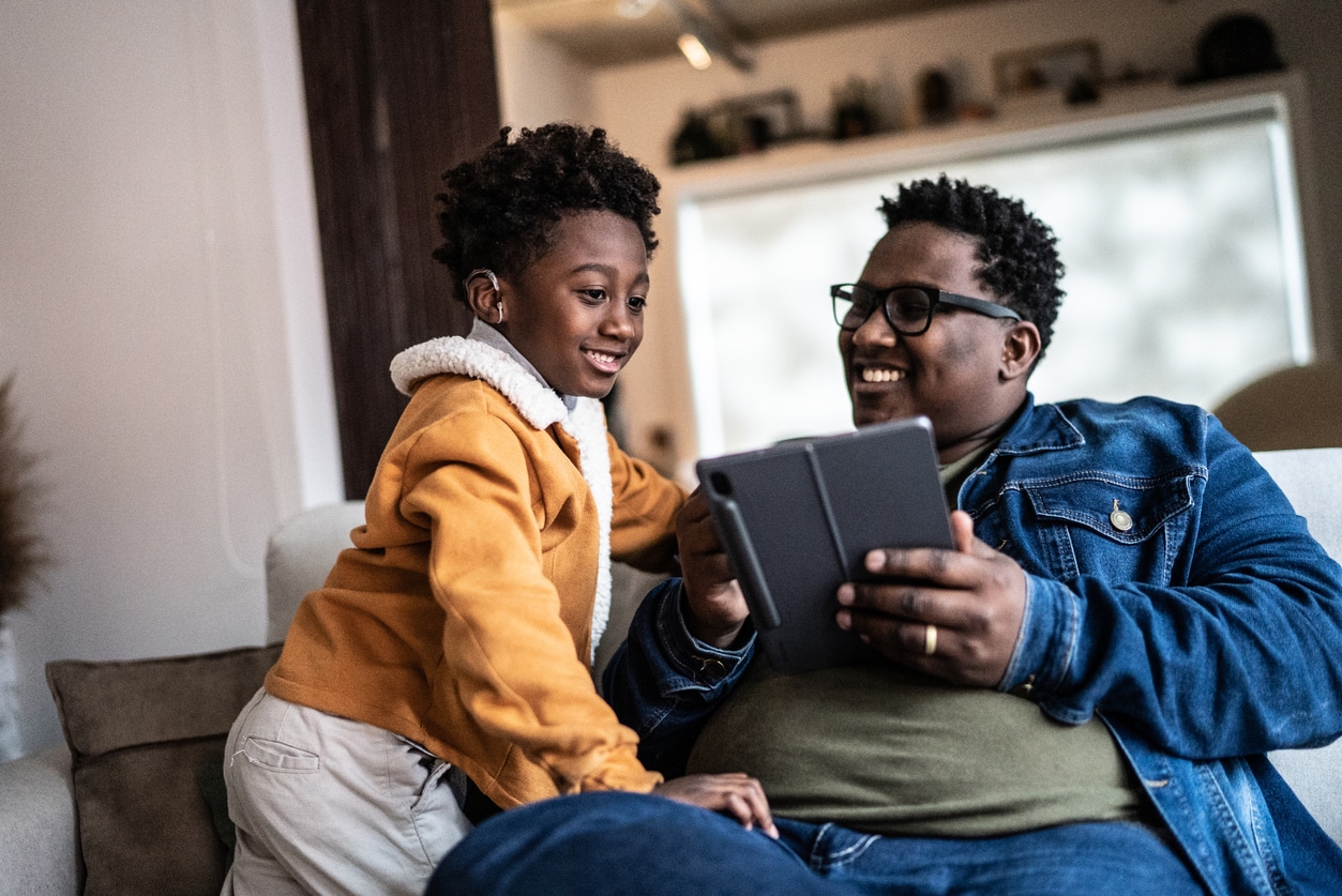 Happy kid wearing a hearing aid looking at a phone with his dad