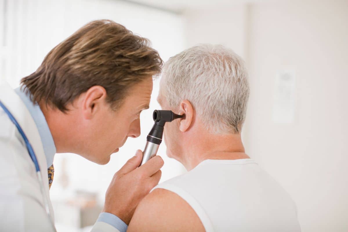 male doctor looking into older male patients ear using an otoscope