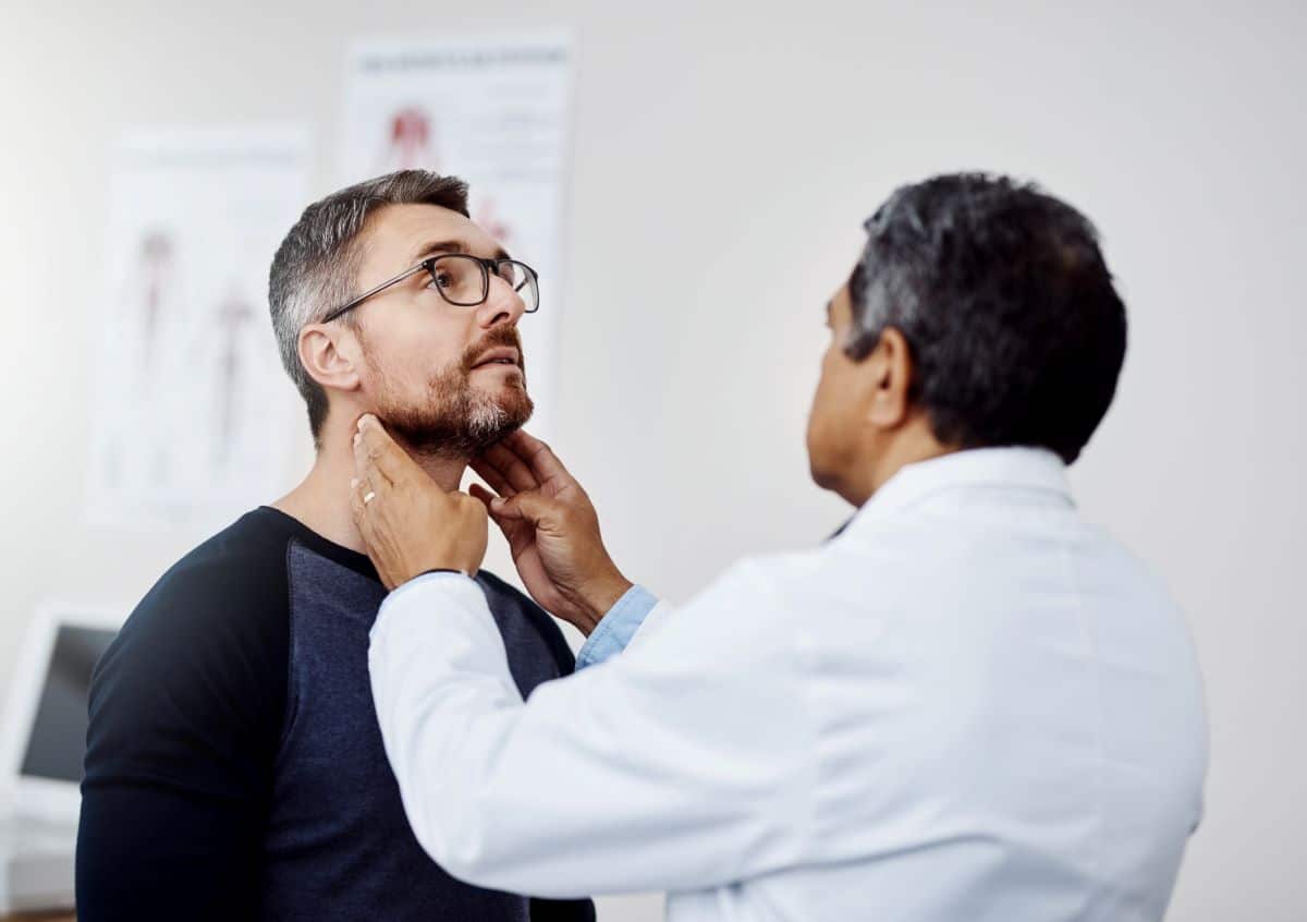 Doctor feeling the throat of a patient in a clinical setting. 