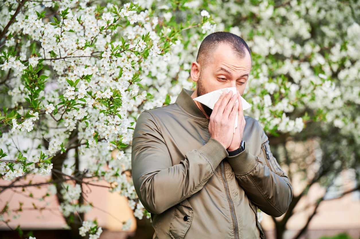 Man blowing his nose around floral trees in the park