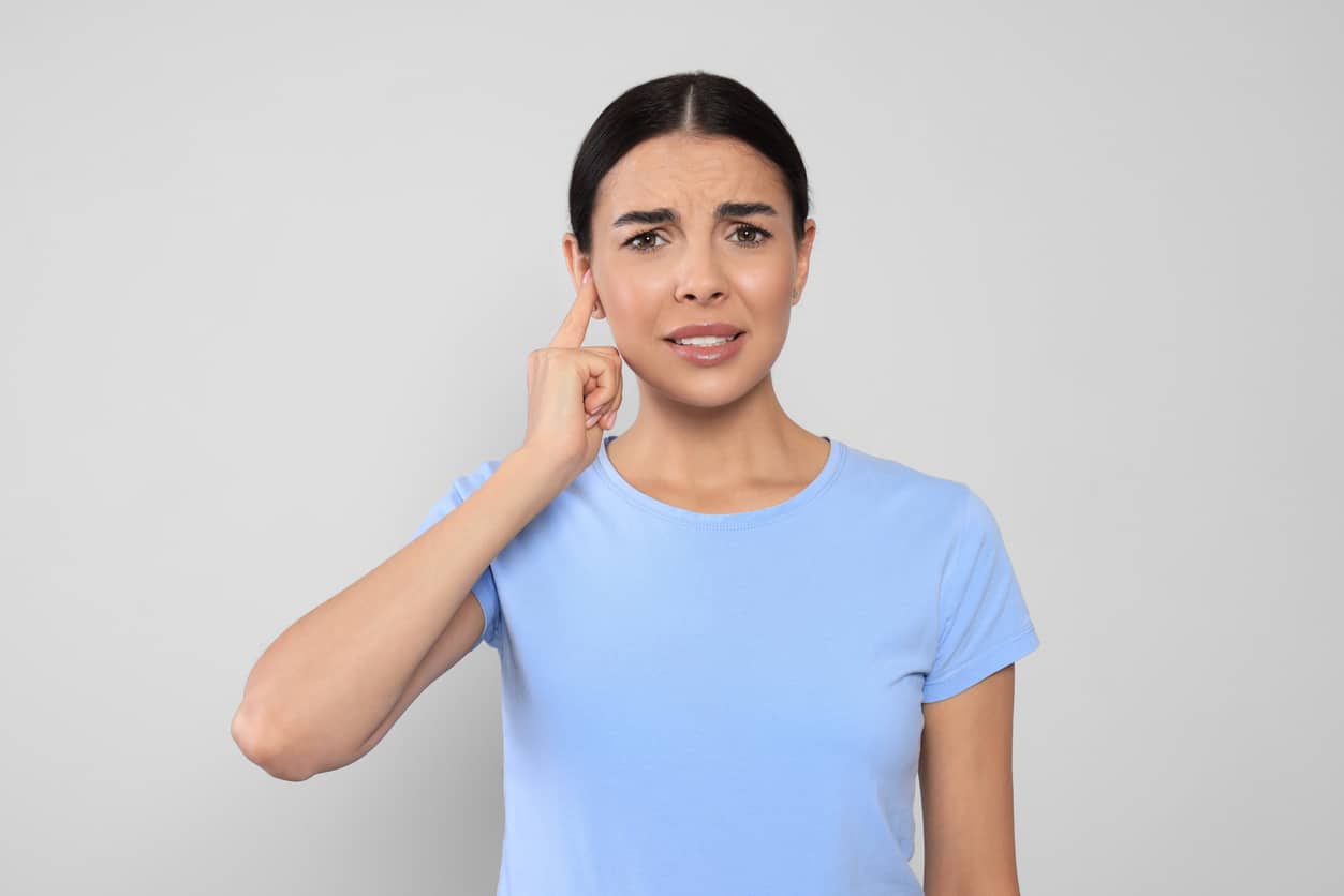 Woman pointing to her ear looking concerned