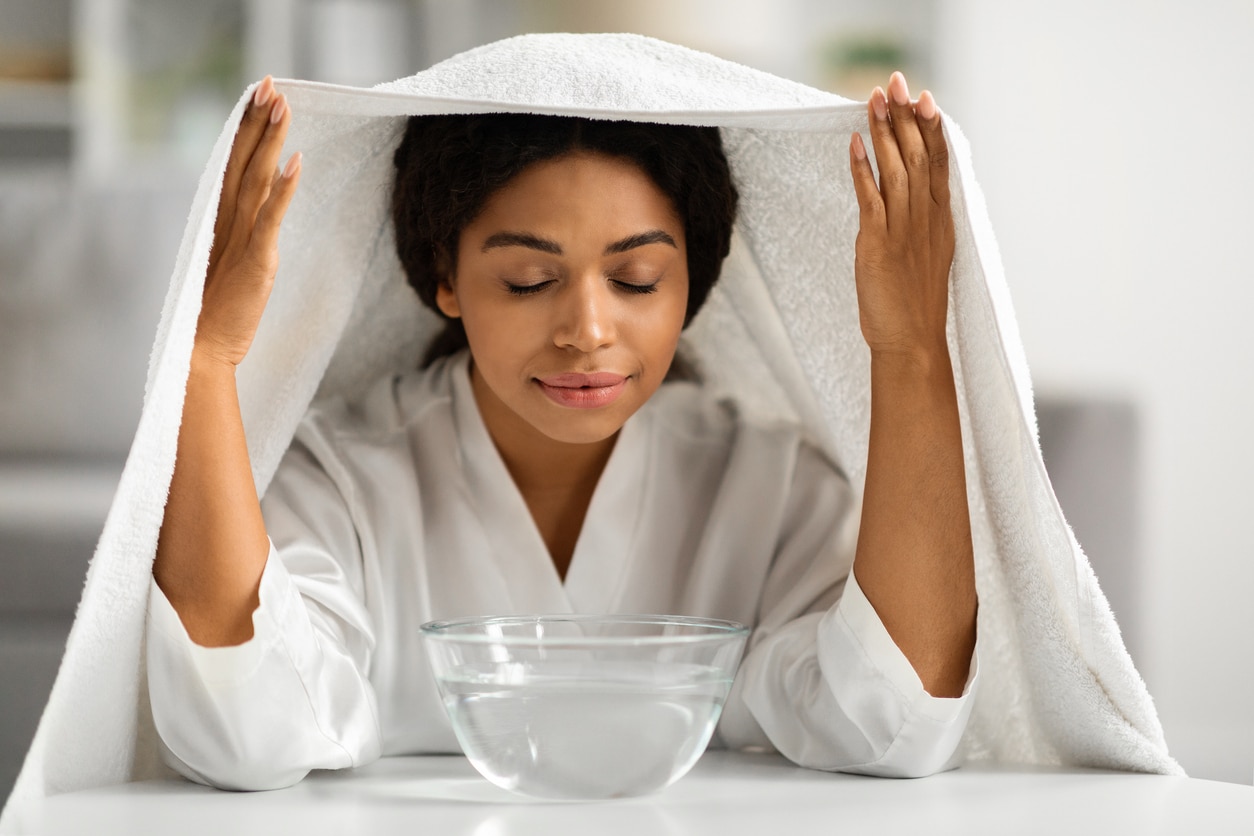 Woman breathing in steam from a large bowl.